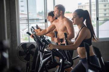 Group of young shirtless man and woman in sportswear working on elliptical machine for cardio...