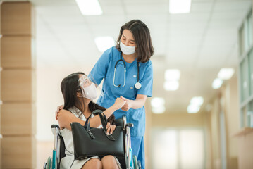 Smiling young female doctor in scrub and covid-19 face mask in conversation with patient sitting in...