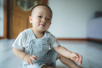 Cute little Asian new born baby boy toddler in comfortable clothing learning to crawl using hands and legs on a white clean marble flooring at home while looking and staring at something in distance
