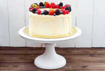 Cheesecake with fresh strawberry, raspberry, blueberry and blackberry, melted white chocolate on rustic wooden cakestand and background
