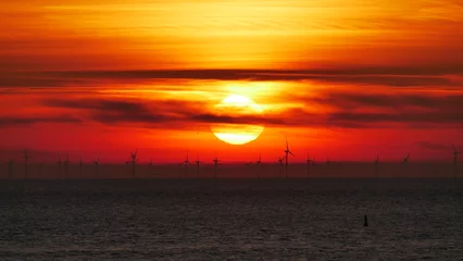 Foto auf Acrylglas Die Sonne versinkt als glühender Ball wie flüssiges Gold dramatisch in der Nordsee mit Silhouetten von Windkraft Anlagen am Horizont © Schattenwanderer