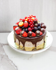 Blue summer cake with fresh berry, cherry, strawberry, raspberry and chocolate sauce on plain grey background