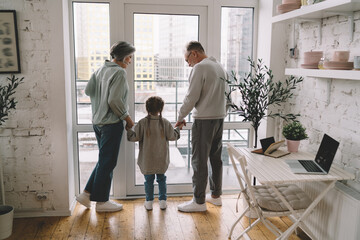 Senior couple holding hands of little girl and standing in doorway at home