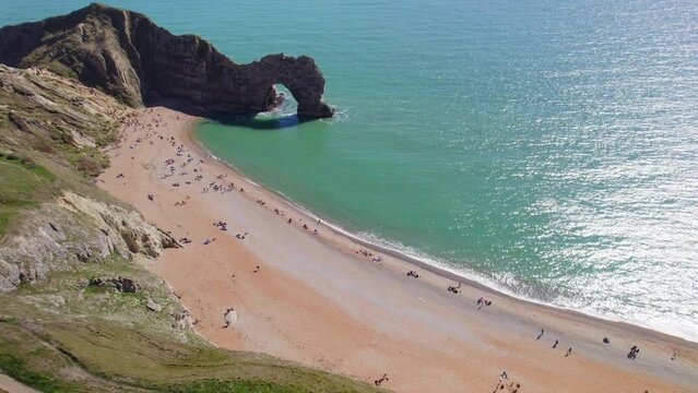 Aerial panning shot of beach and Durdle Door stone arch in Dorset, UK