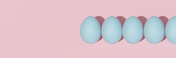 Pastel blue Easter eggs lie in a row isolated on a pink background. The brush paints the Easter egg...