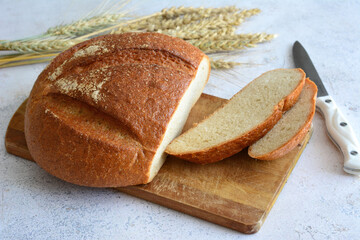 A loaf of bread on a cutting board with wheat ears on the side, close-up 