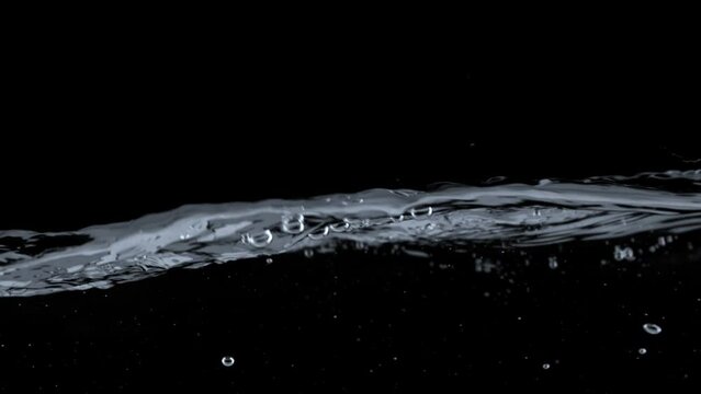 Water splashes and waves on balck background. Slow motion shot of water surface with ripples