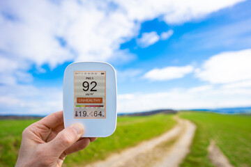 air quality monitor in hand against the background of a summer green field shows the amount of...