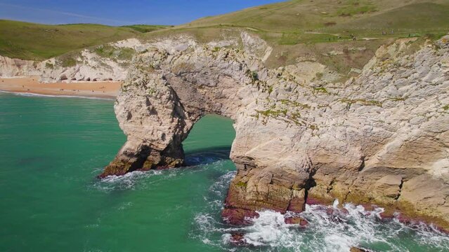 Aerial shot of Durdle Door rock arch looking back towards the beach and tourists, Dorset, UK