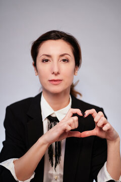 Making heart with hands. Confident business lady in black jacket posing on isolated background. Cheerful manager woman in dark suit looking at camera making heart shape. High quality vertical photo