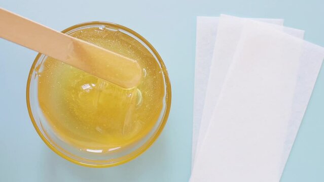 Liquid yellow sugar paste, wooden spatula, depilatory strips on a blue background. Removing unwanted hair. Sugaring. Depilation. Epilation. Beauty. Top view.