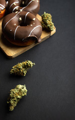 Dry buds of medical marijuana close-up with donuts covered with chocolate icing, sprinkled with nut...