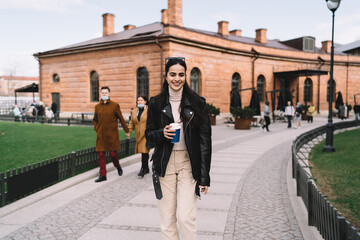 Fototapeta premium Cheerful woman with takeaway coffee walking on street