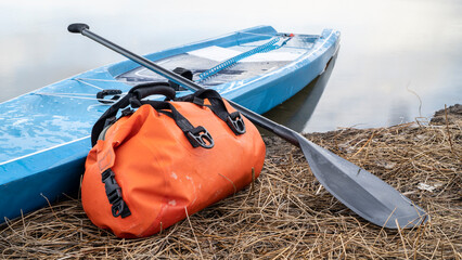 touring stand up paddleboard with a paddle and safety leash on a lake shore, early spring in...
