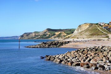 View looking West across the bay towards the beach and cliffs of the Jurassic Coast with town buildings to the rear, West Bay, Dorset, UK.