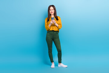 Full length photo of adorable pretty woman wear yellow shirt typing message modern device isolated blue color background