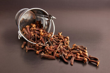 A small metal bucket filled with clove spices on a black background.