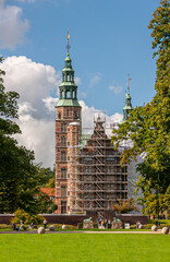 Obraz premium Copenhagen, Denmark - September 13, 2010: Green landscape under blue cloudscape. Scaffold Rosenborg Slot SW entrance facade in Kongens Have. Brown stone tower with green bronze steeple