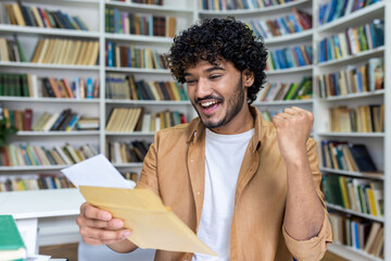 Young student received letter with good exam results and university admission confirmation, hispanic man with curly hair celebrating successful achievement holding hand up close up. - Powered by Adobe