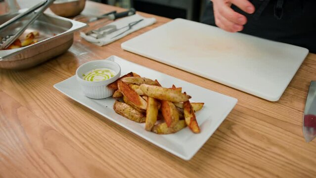Professional chef adds sour cream sauce to baked potato wedges in the process of preparing a healthy meal