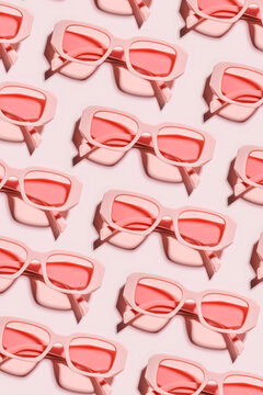 Pattern of pink color sunglasses on pink background at sunlight with shadow. Summer fashion eyeglasses with rose colored glass. Summer vacation, summer rest concept. Minimal style flatlay