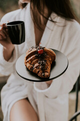A woman in a white bathrobe eats a croissant and drinks coffee in a hotel in the mountains.Resort...