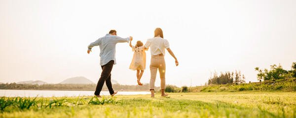 Back view of Happy Asian family walking and playing together in a scenic garden, with a beautiful sunset in the background and a feeling of fun and enjoyment, Family day - Powered by Adobe