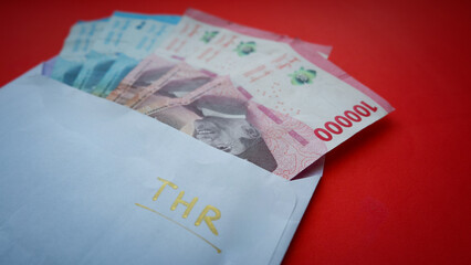 Indonesian money or IDR in the envelope with THR text isolated on red background. THR is holiday allowance in Eid Al-fitr or lebaran day