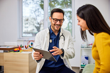Obraz premium A smiling male pediatrician holding a digital tablet and talking with a child's mother.