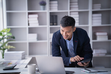 Portrait of Smiling young male employee feel euphoric sitting at his desk using smart phone at...