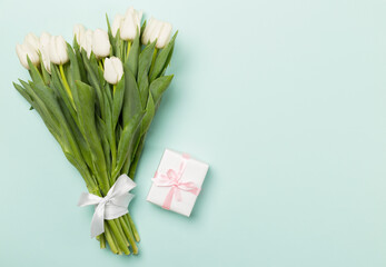 White tulip bouquet and gift box on color background, top view