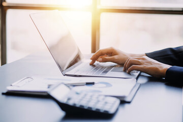 Asian Business woman using calculator and laptop for doing math finance on an office desk, tax, report, accounting, statistics, and analytical research concept
