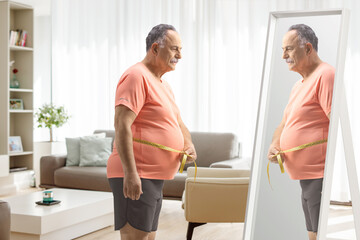 Mature man measuring waist in front of a mirror