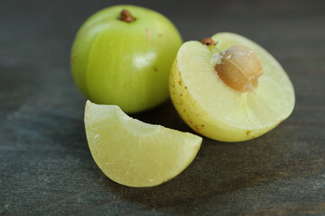Closeup of Fresh Amla Berry Cross Section with Whole Fruit on Black Wooden Background
