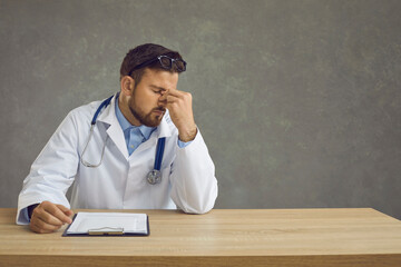 Medical everyday life. Exhausted male doctor sitting at the table after a hard day work. Sad doctor...