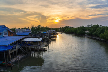 Many fishing community houses have fishing boats moored next to the river that leaves estuary of the Gulf of Thailand in the evening.