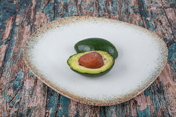 Avocado cut in half in porcelain plate on wooden background.