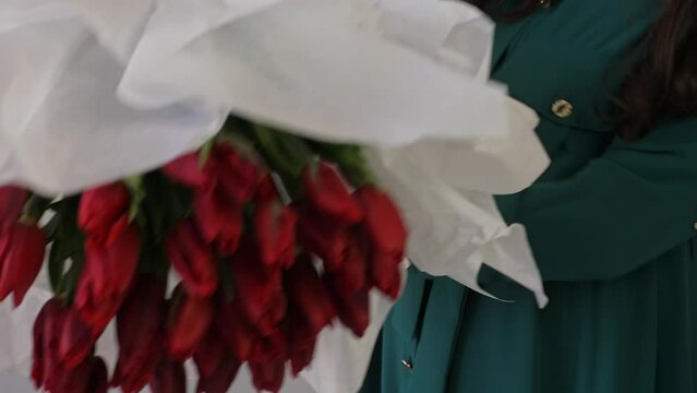 Caucasian lady florist collects a lush bouquet of tulips. A professional makes a fresh bouquet. Small business. A woman crumples paper (Crepe) and wraps a bouquet of tulips in it