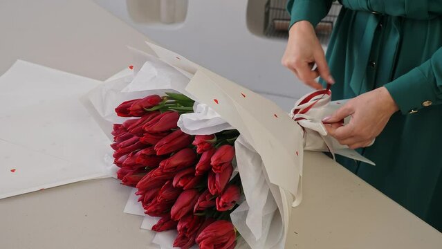 Caucasian lady florist tying a ribbon at the base of bouquet of tulips. A professional makes a fresh bouquet. Small business.