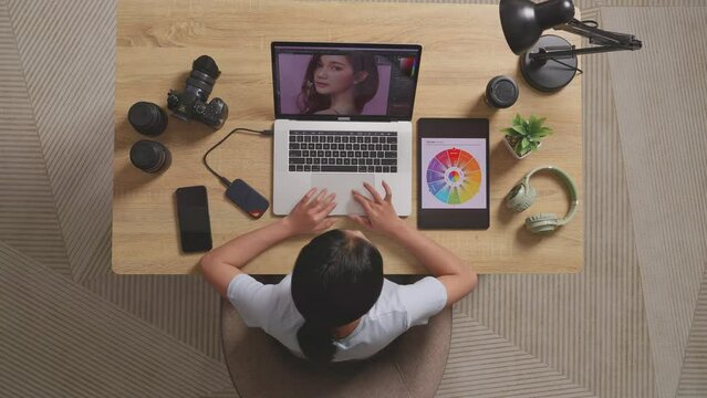 Top View Of A Woman Editor Looking At The Color Schemes On A Tablet While Sitting In The Workspace Using A Laptop Next To The Camera Editing Photo Of A Woman At Home
