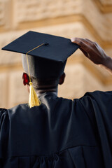 Portrait closeup of black student in graduation mantle and hat standing with back outdoors and...