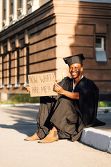 Happy black guy sitting with cardboard poster on street looking for job. University or college...