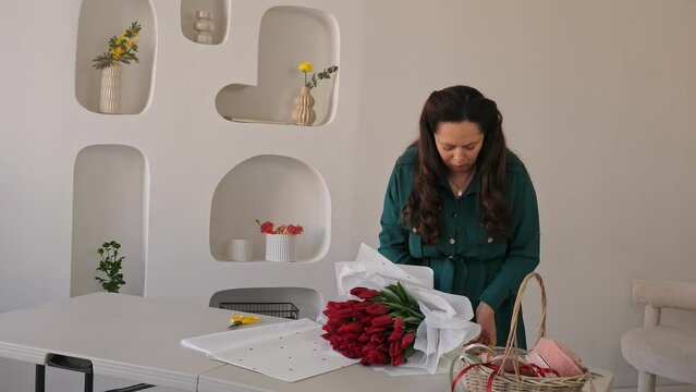Caucasian lady florist collects a lush bouquet of tulips. A professional makes a fresh bouquet. Small business.