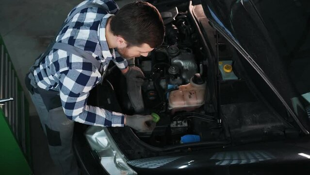 Top view, hood is opened. Man is repairing the car at a service station.