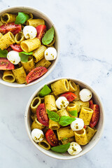Rigatoni pasta with pesto, tomatoes and mozzarella in white bowl. Italian cuisine concept.