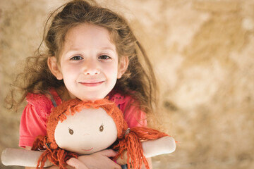 An adorable cute little white Caucasian girl lovingly holding a cherished rag doll with ginger hair