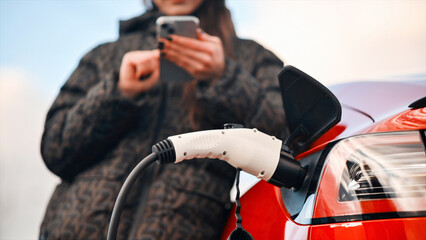Fototapeta na wymiar Woman using smartphone near charging electric car