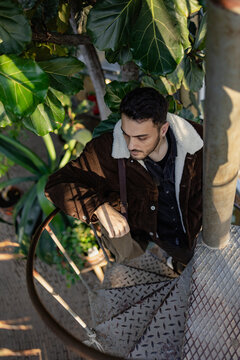 A Handsome Man Climbing Up Stairs. There Is Green Plants Behind Him.