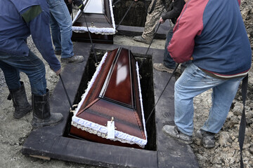 Communal workers lift the coffins into graves during the funeral ceremony