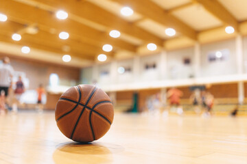 Classic Orange Basketball Ball On Wooden Sports Court. Junior Level Basketball Players Playing Game in Blurred Background. Basketball Training Background.